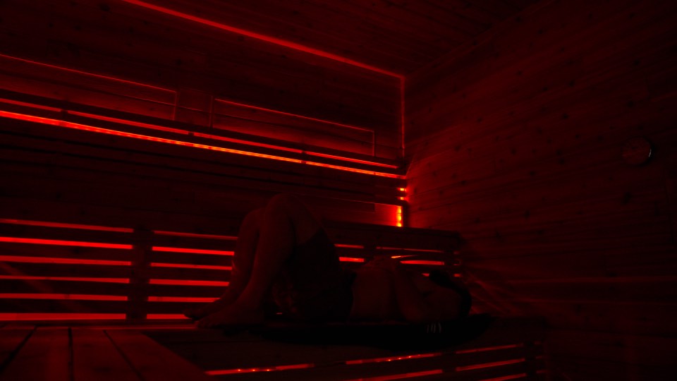 Someone sitting on the top bench of the sauna in low red light