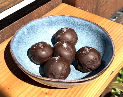 Chocolate-coated protein balls with flaky salt, in a blue bowl in the sun