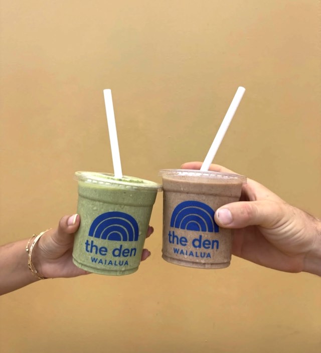 Two Den Waialua smoothies held up against a warm ochre wall