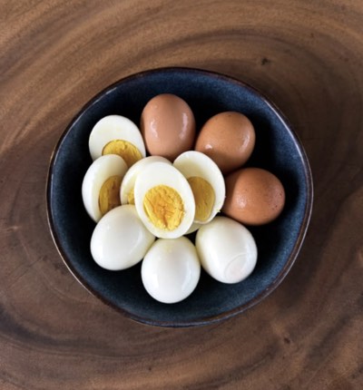 A bowl of hard-boiled eggs, some halved, on a wooden counter