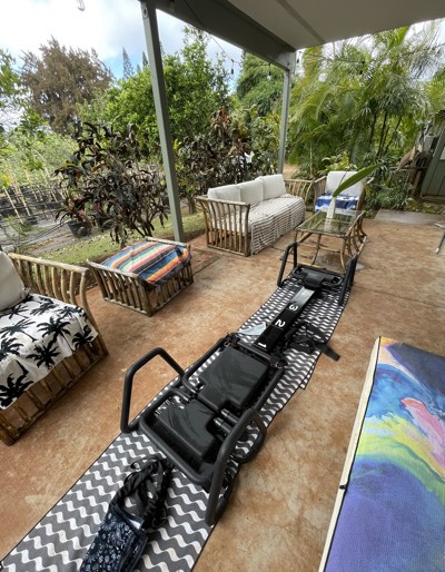 A single reformer on a patterned mat on the back deck, garden beyond